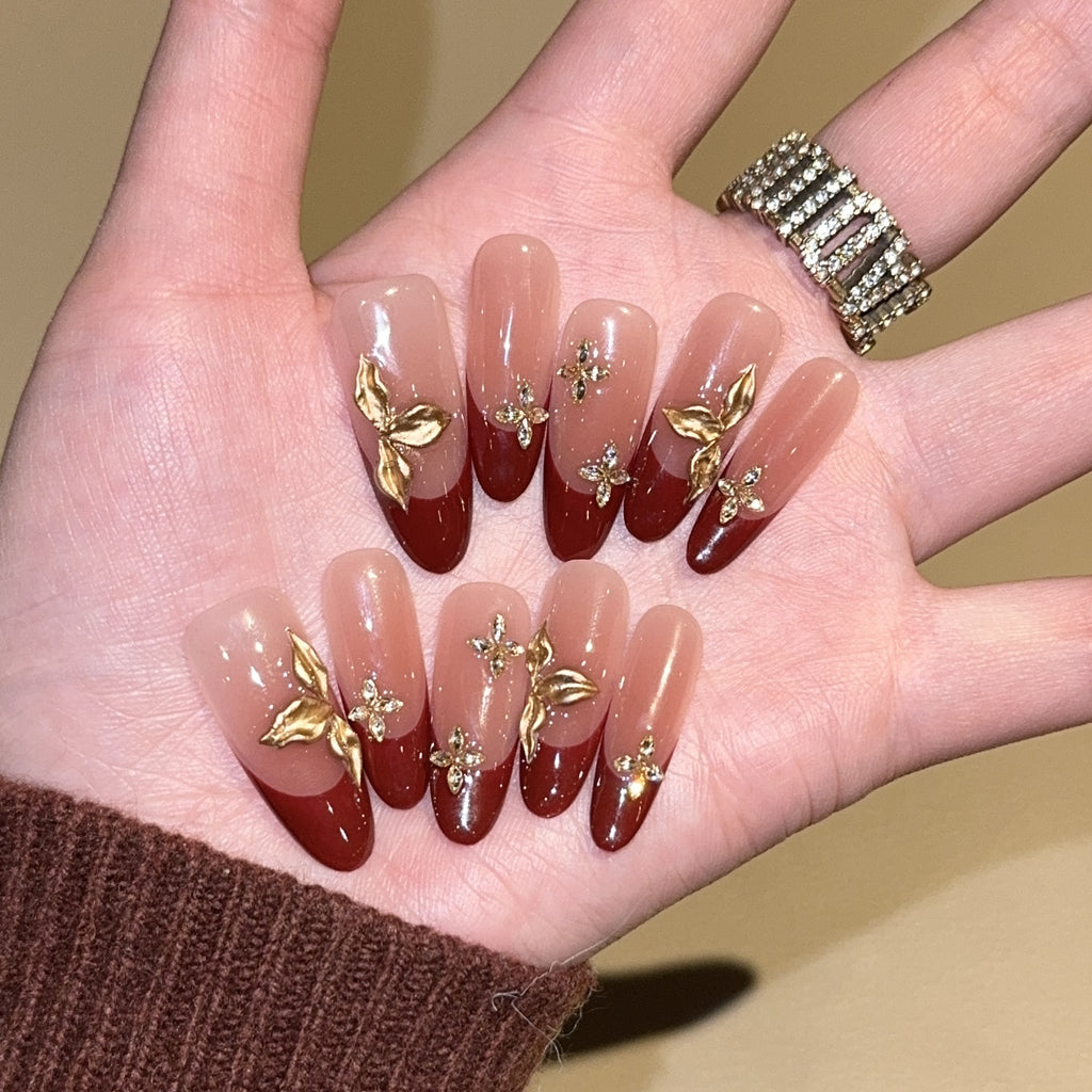Burgundy French oval press-on nails with gold botanical embellishments
