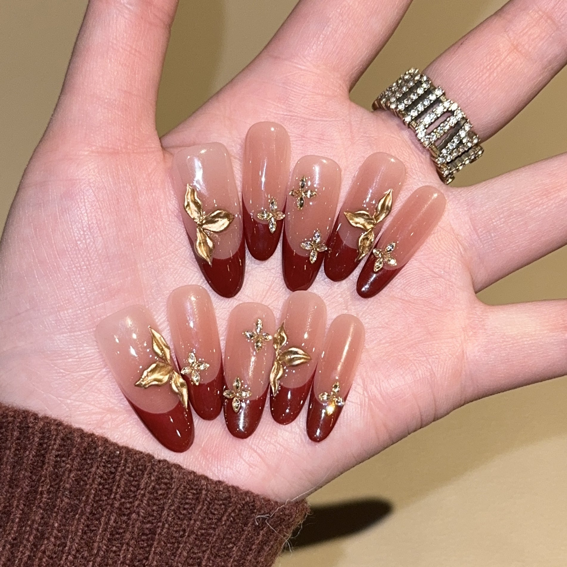 Burgundy French oval press-on nails with gold botanical embellishments