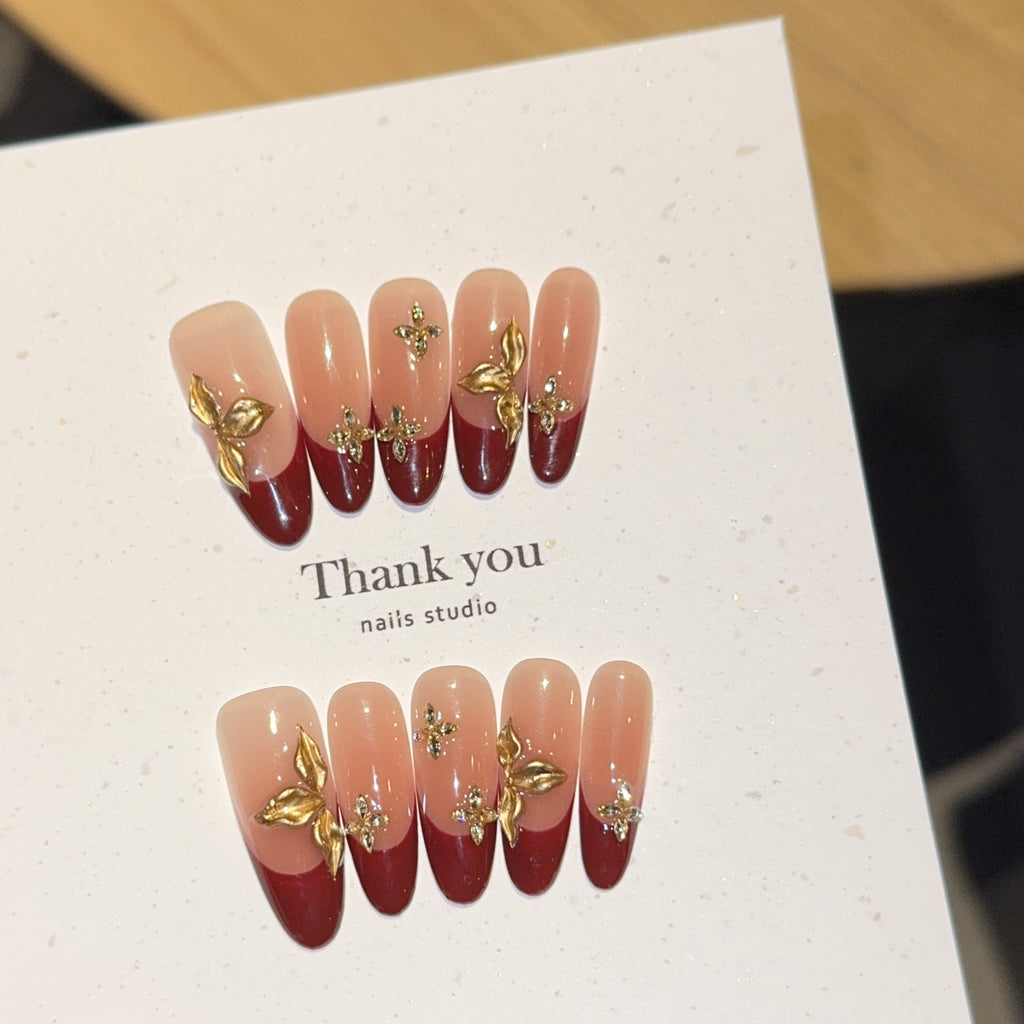 Burgundy French oval press-on nails with gold botanical embellishments