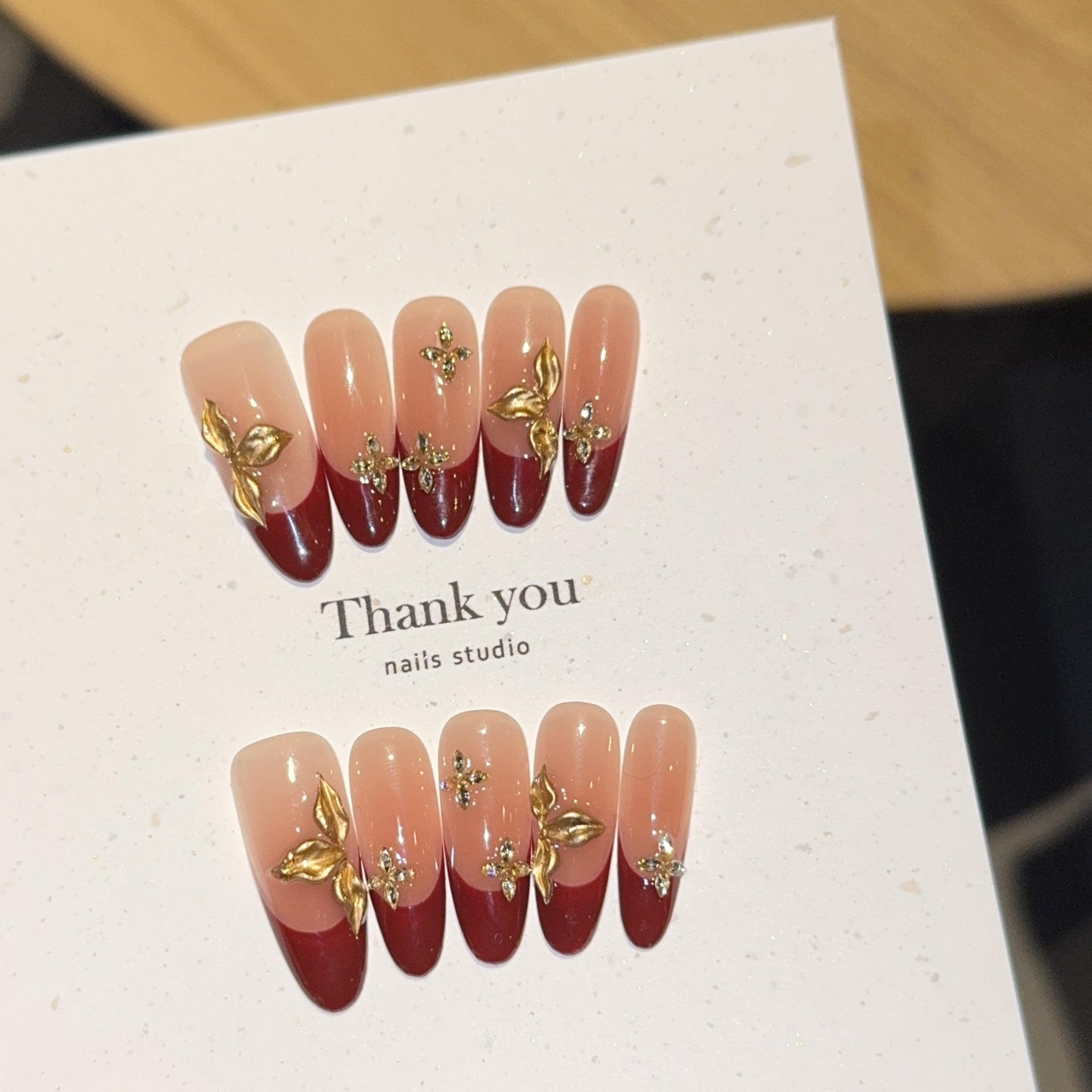 Burgundy French oval press-on nails with gold botanical embellishments