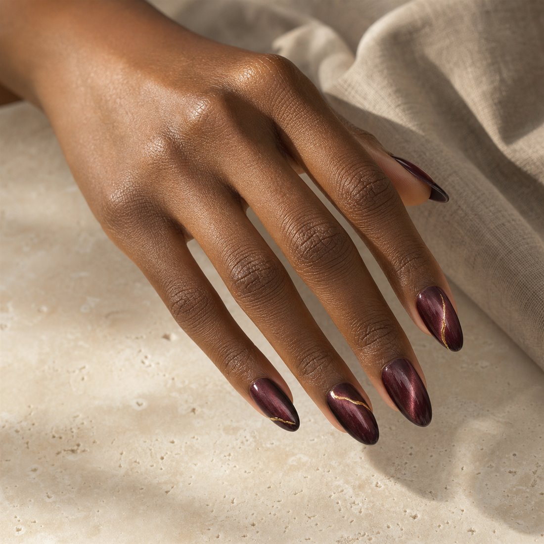 Deep brown hand wearing burgundy almond press-on nails