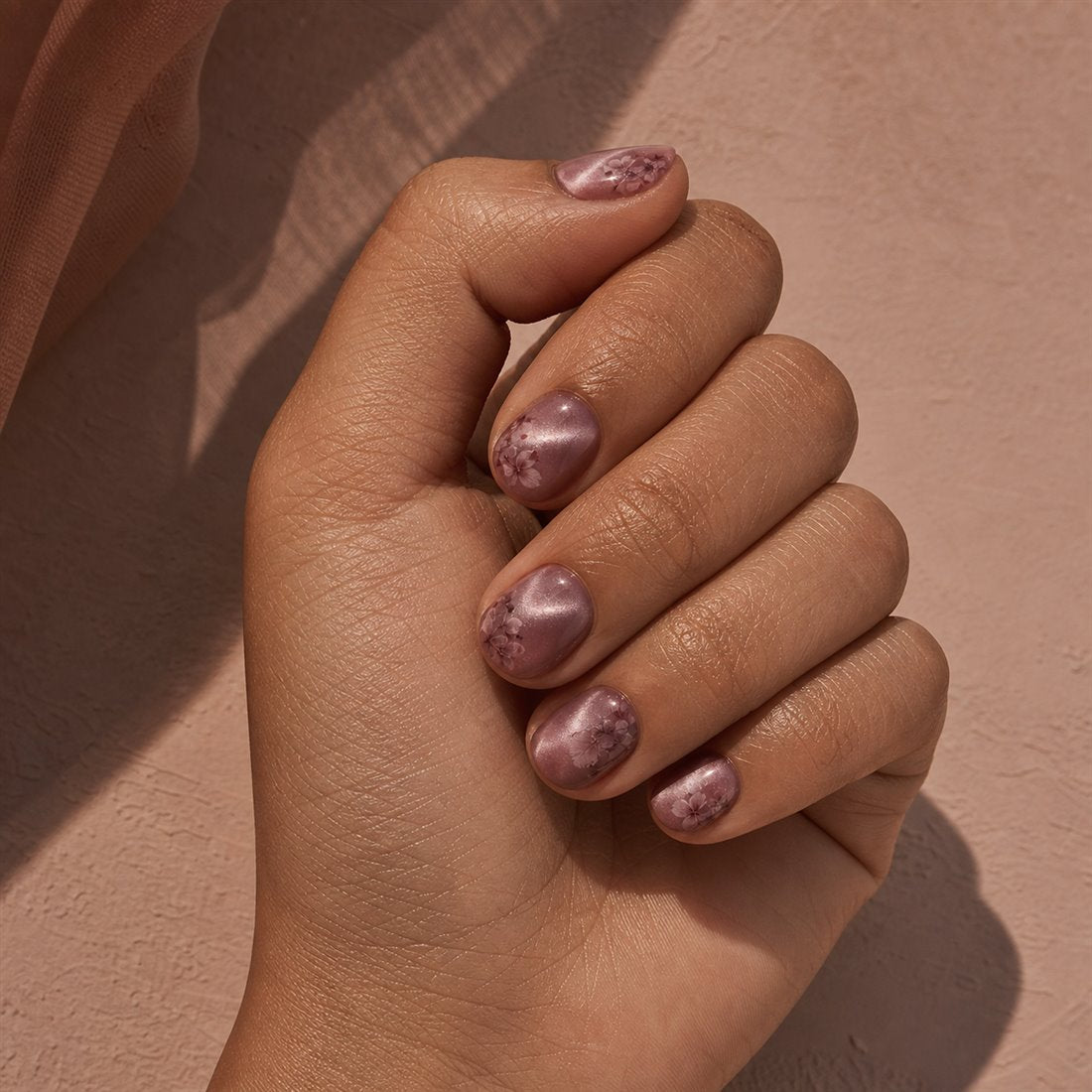 Olive-toned hand wearing short blush floral cat-eye press-on nails